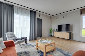 A modern living room with a sofa, a coffee table, a TV, and a radiator. - Faro Beach Apartments with parking (Gdańsk)