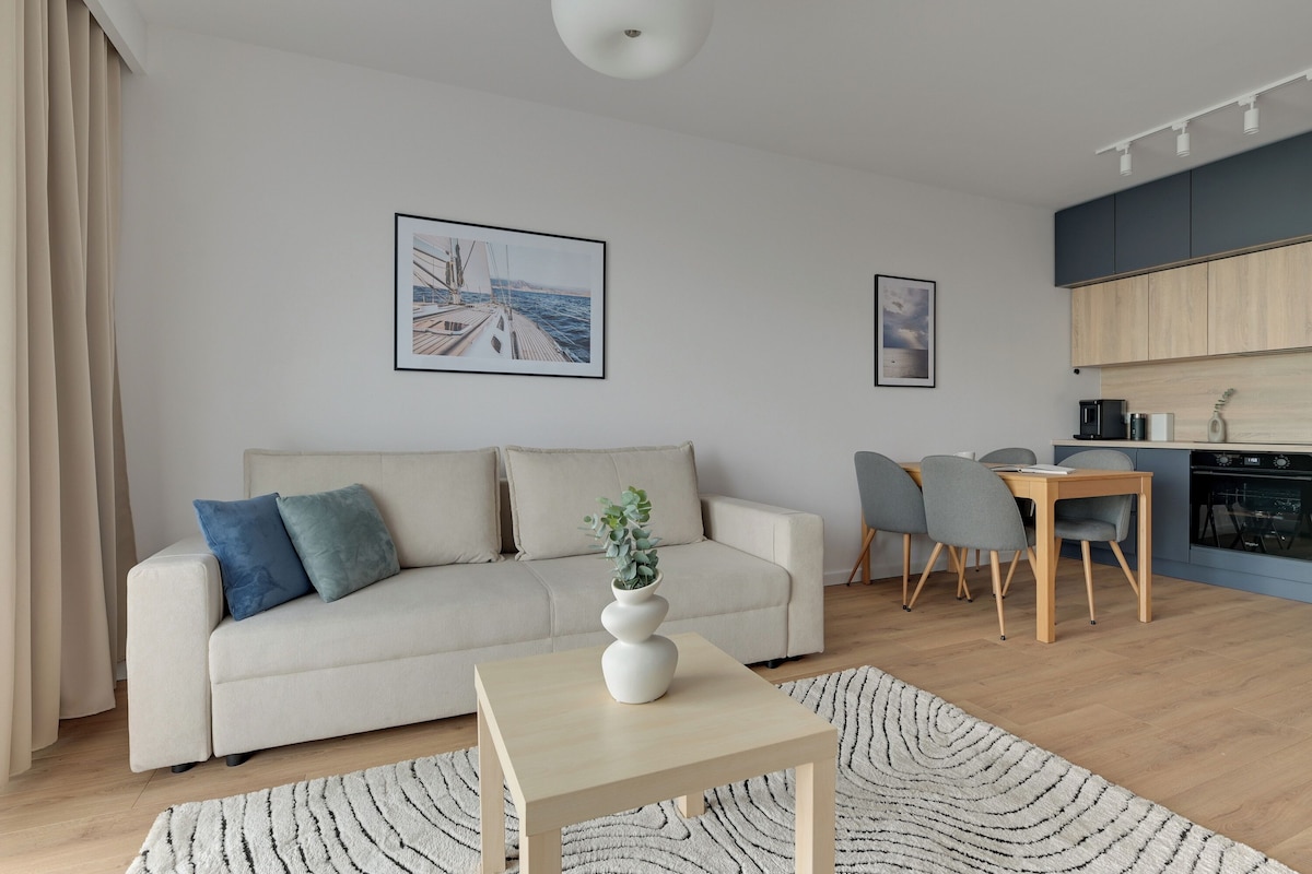A modern living room with a sofa, a coffee table, and a dining area with chairs. There are two framed pictures on the wall.