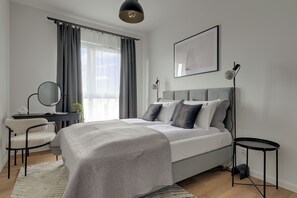A modern bedroom with a bed, bedside tables, a desk, and a chair. - Faro Beach Apartments with parking (Gdańsk)