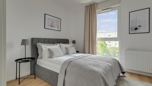Un dormitorio moderno con una cama, una mesita de noche, una lámpara y dos cuadros en la pared.