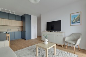 Uma sala de estar moderna com televisão, sofá, mesa de jantar e cozinha ao fundo.