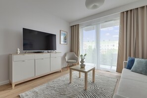 A modern living room with a flat-screen TV, a sofa, a coffee table, and a balcony with curtains.