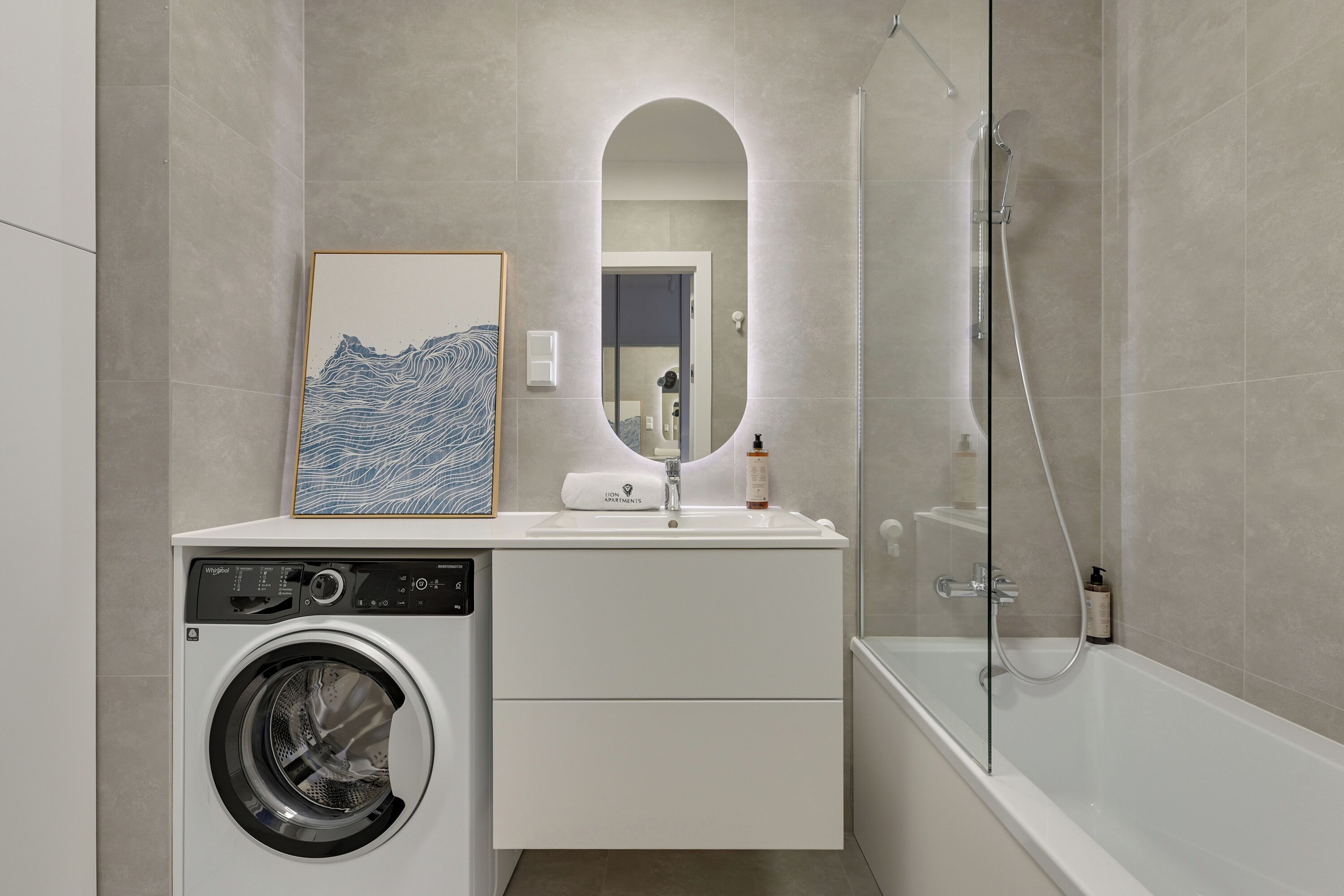 A modern bathroom with a washing machine, a sink, a mirror, and a glass-enclosed shower.