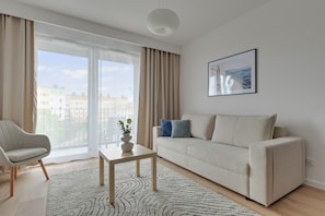 Una sala moderna con un sofá, una silla, una mesita con una planta y un ventanal con cortinas.