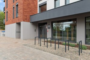 Edificio moderno con fachada de ladrillo, acceso de vidrio y una zona pavimentada con bancos.