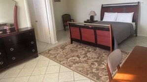 Quarto com cama, mesa de cabeceira, luminária, cadeira, cômoda e uma porta.