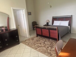 A bedroom with a bed, bedside table, lamp, chair, dresser, and a door. - Charming Bed & Breakfast with amazing ocean views nestled in the hills  of Escap (Micoud)