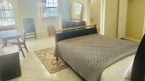 Quarto com cama, escrivaninha, cadeira, guarda-roupa e banheiro visível por uma porta aberta.
