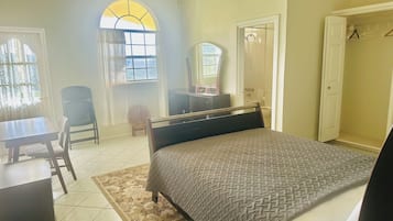 A bedroom with a bed, a desk, a chair, a wardrobe, and a bathroom visible through an open door.