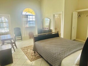 A bedroom with a bed, a desk, a chair, a wardrobe, and a bathroom visible through an open door. - Charming Bed & Breakfast with amazing ocean views nestled in the hills  of Escap (Micoud)