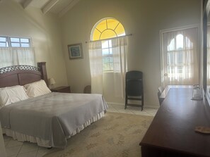 A bedroom with a bed, a chair, a table, and a window with curtains.