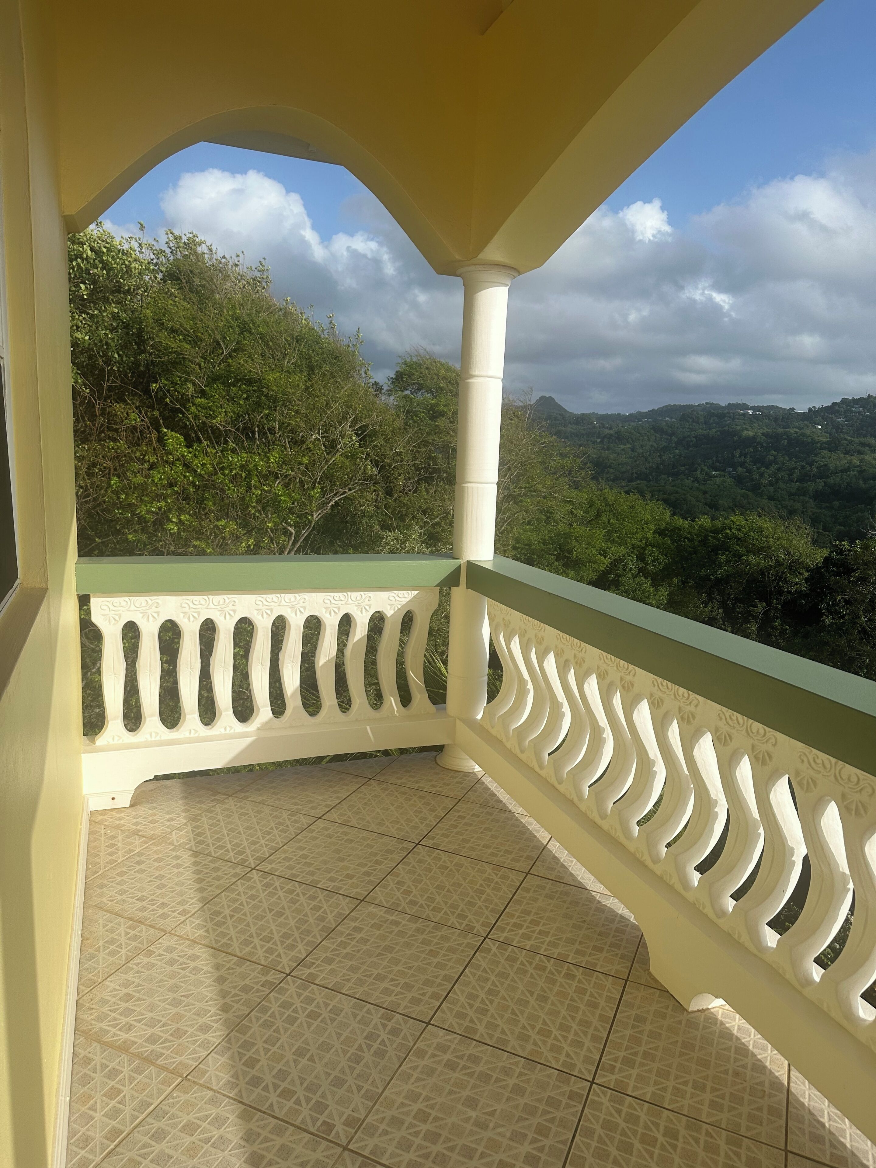 A balcony with a patterned floor, a white balustrade, and a view of a hilly landscape.