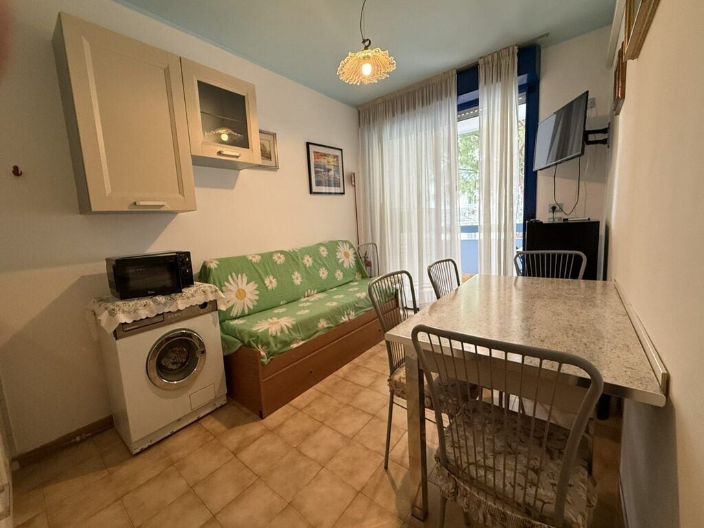 Un espacio habitable compacto con sofá, lavadora, mesa de comedor con sillas y televisor.
