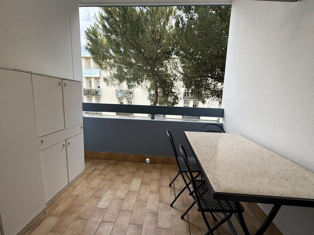 Un balcon avec une table et des chaises, une vue sur les bâtiments et les arbres, et un sol carrelé.