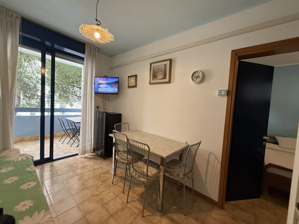 A room with a dining table, chairs, a television, and a sliding glass door leading to an outdoor area.