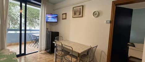 Una habitación con una mesa de comedor, sillas, un televisor y un ventanal corredero que da a un espacio exterior.