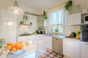 Ett modernt kök med vita köksskåp, en diskmaskin i rostfritt stål, en gasspis och ett urval av olika frukter och grönsaker på bänkskivan.