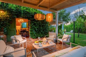 Eine Terrasse im Freien mit Korbmöbeln, einem Tisch mit Obstschale und einer mit Grünpflanzen bewachsenen Backsteinmauer.