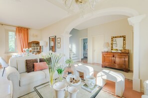 A spacious living room with a white sofa, a glass coffee table, and a dining area with a table set for four. - A Peaceful 3-Bedrooms Oasis In Orentano (Orentano)