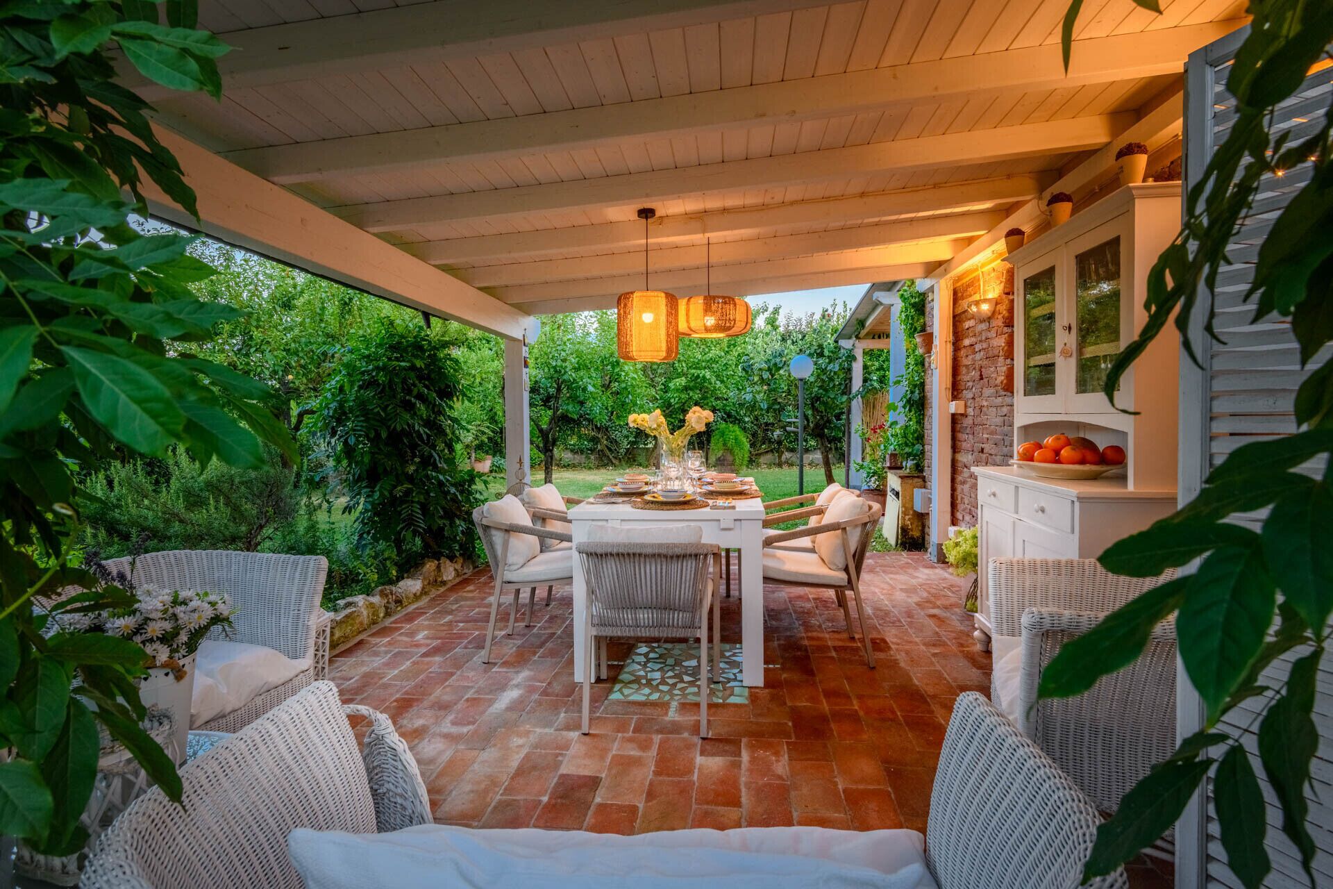 Eine Terrasse im Freien mit Tisch und Stühlen, umgeben von Pflanzen und einem Pflasterboden.