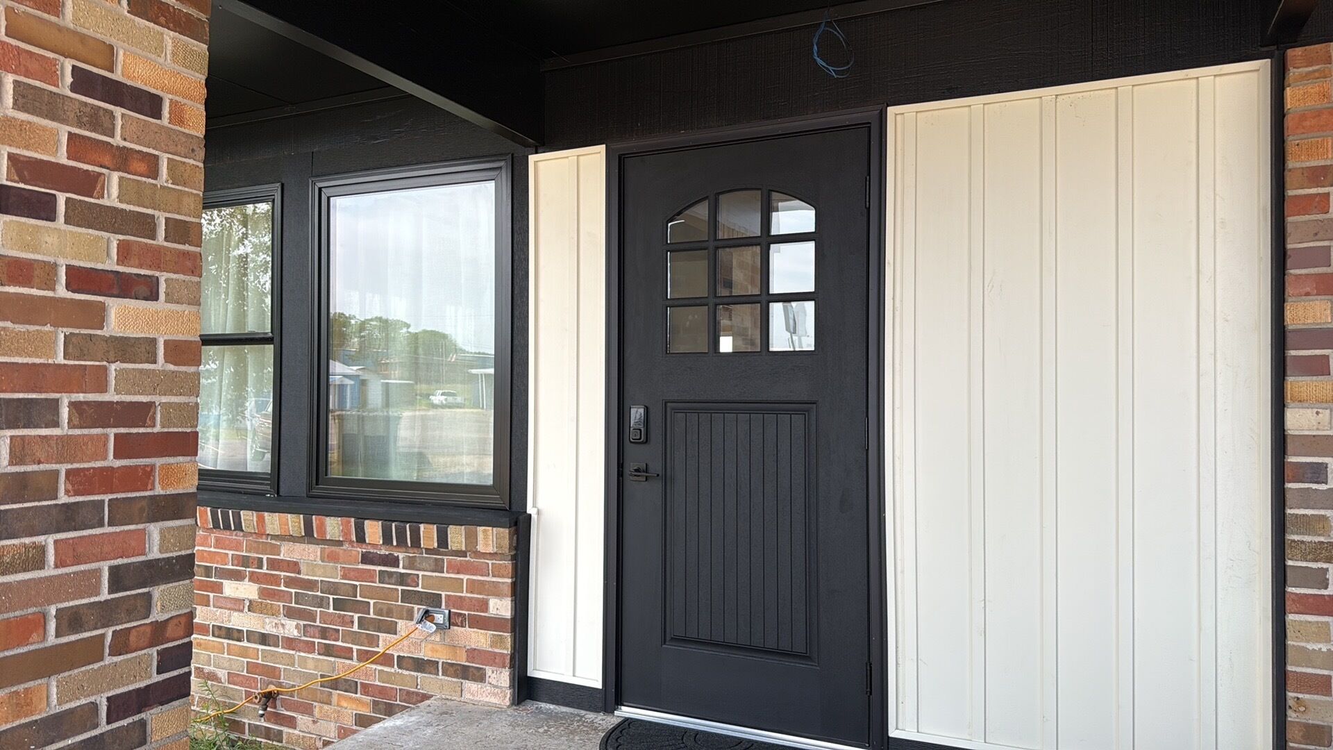 A black door with a window above it, a white door to the right, and a brick wall on the left.