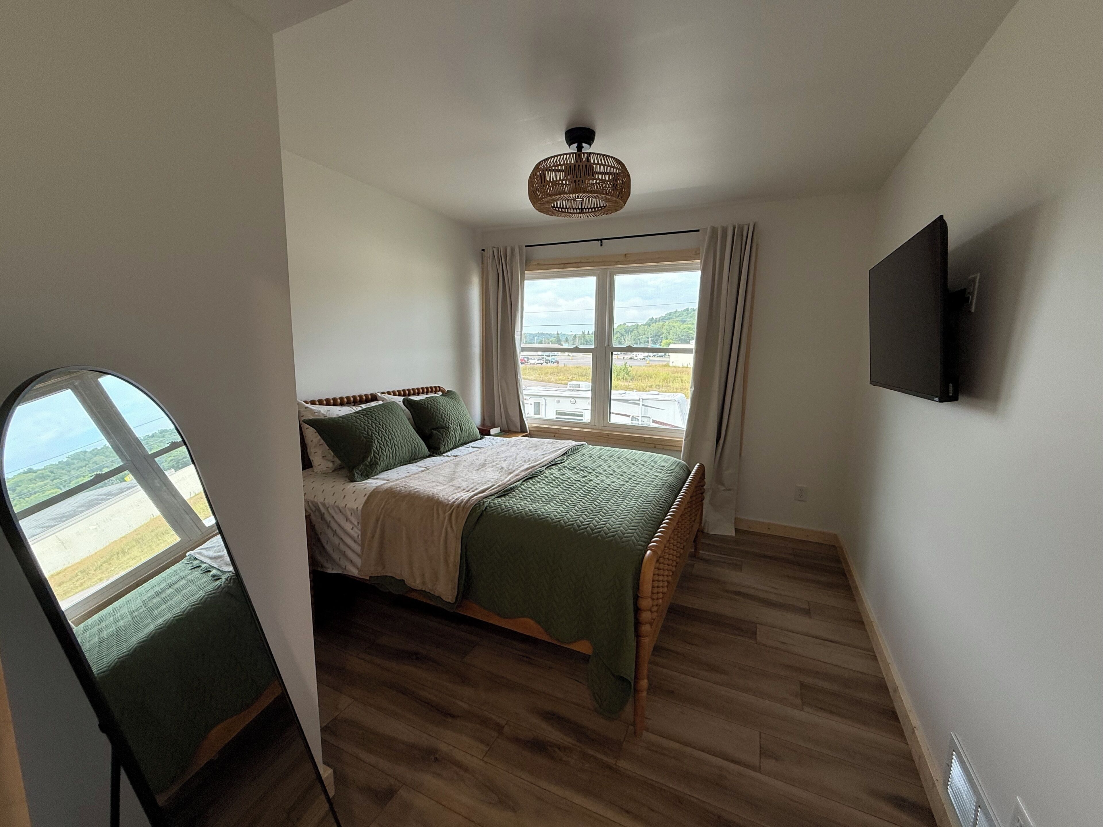 A bedroom with a bed, a window, a television, and a view of the outdoors.