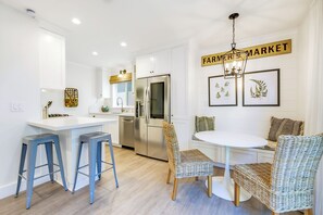 A modern kitchen with a white countertop, stainless steel appliances, and a dining area with wicker chairs and a white table. - Great 4 Families, Walk 2 Beach and Bay W/Parking! (Newport Beach)