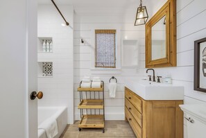 Un bagno moderno con una parete rivestita di piastrelle bianche, un mobile lavabo in legno, una vasca da bagno e un porta asciugamani.