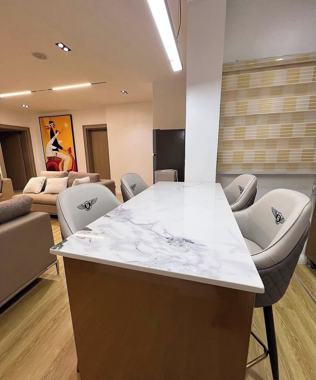 A modern living room with a marble-top dining table, leather chairs, a sofa, and a large abstract painting on the wall.