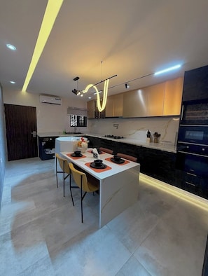 A modern kitchen with a central island, recessed lighting, and a built-in oven. - Hossana Apartment (Port Harcourt)