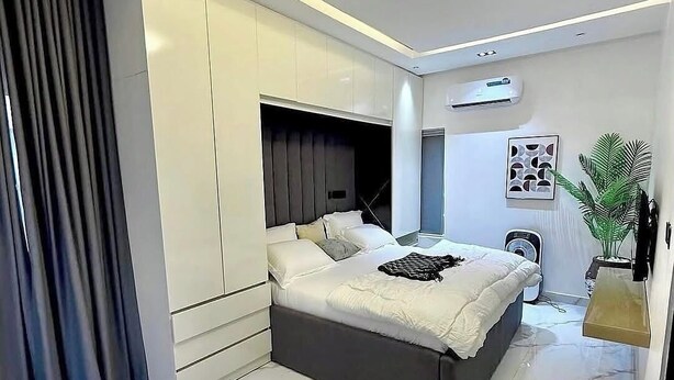 Quarto moderno com cama grande, roupeiro embutido e luminária no teto.