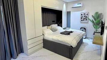 A modern bedroom with a large bed, built-in wardrobe, and a ceiling light fixture.