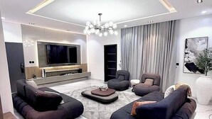 Uma sala de estar moderna com uma televisão grande, sofás escuros e um lustre.