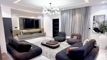 A modern living room with a large TV, dark sofas, and a chandelier.
