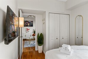 A hotel room with a bed, a TV, a desk with a chair, a plant, and a wardrobe.