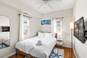 A hotel room with a bed, a nightstand, a lamp, a wall-mounted TV, and a ceiling fan.