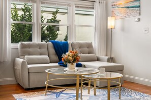 A living room with a sofa, two glass tables, a vase of flowers, and a painting on the wall.