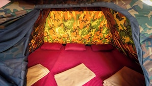 A tent with a camouflage interior, a red bed with pillows, and a beige blanket.