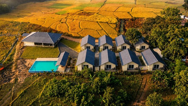 A residential area with multiple houses, a swimming pool, and terraced fields in the background.