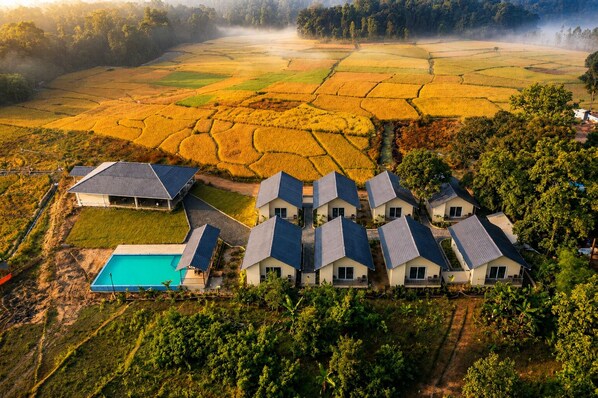 A residential area with multiple houses, a swimming pool, and terraced fields in the background.