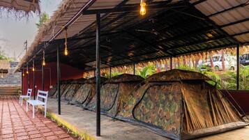 A row of camouflage tents under a covered area with hanging lights, a brick pathway, and a vehicle in the background.