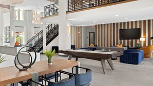 Eine moderne Hotelhalle mit Billardtisch, Sitzgelegenheiten und einer Treppe.