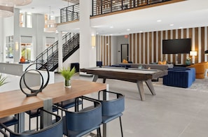 En modern hotellobby med ett biljardbord, en sittgrupp och en trappa.