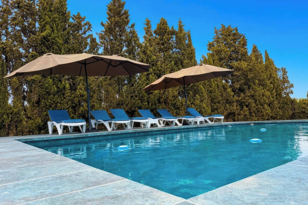 A swimming pool with lounge chairs and umbrellas, surrounded by trees.