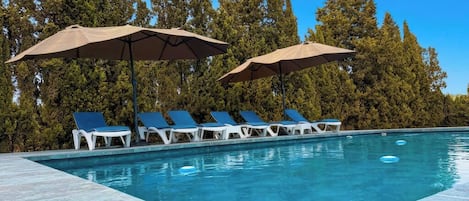 A swimming pool with lounge chairs and umbrellas, surrounded by trees.