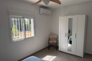 A room with a bed, a wardrobe, a chair, and a window with a view of greenery. - Villa Perfecta: A 5-bedroom villa with a pool, just 30 minutes from Valencia! (Llíria)