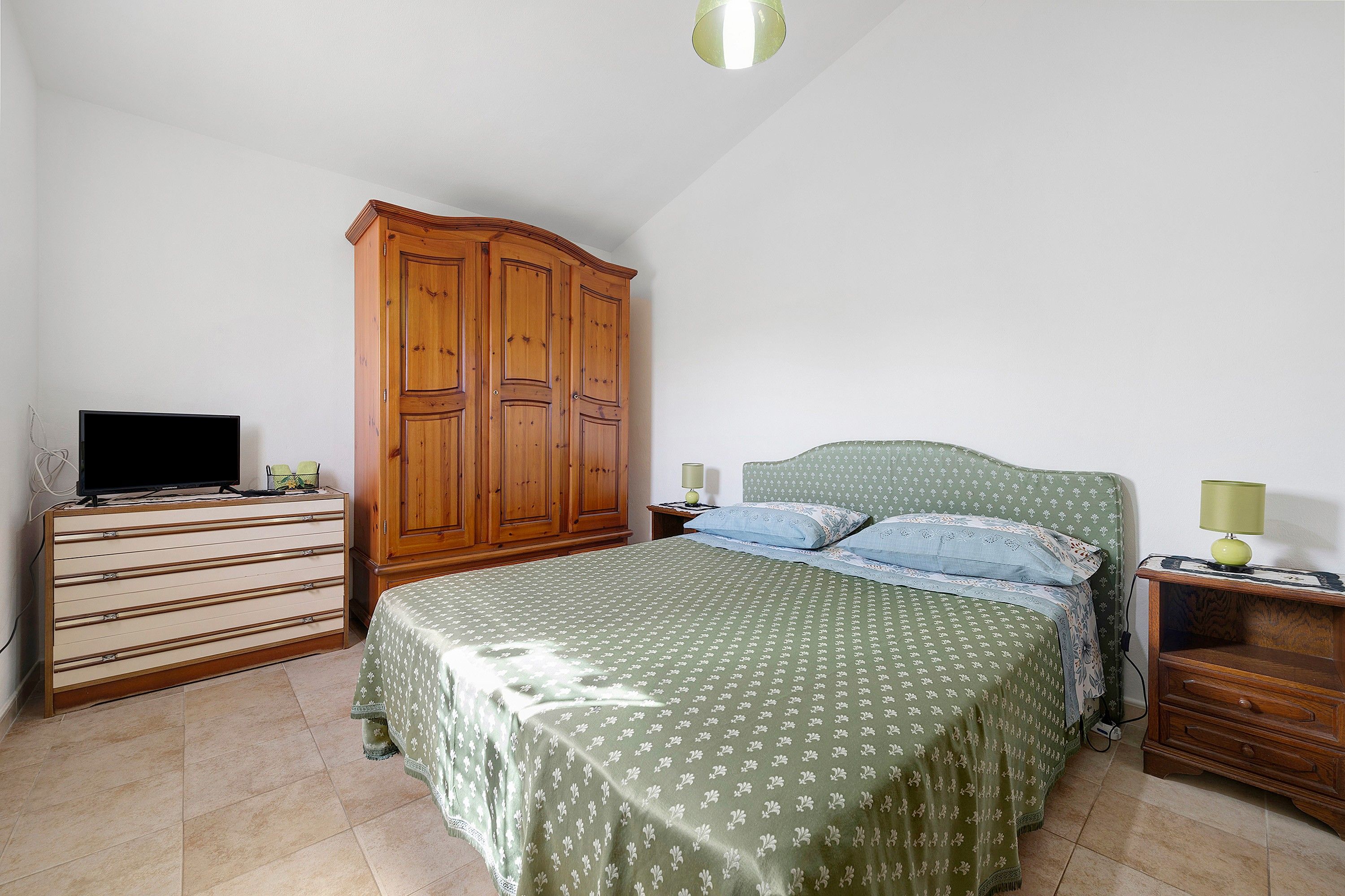 Een slaapkamer met een bed, een houten garderobe, een dressoir, een televisie en een lamp.