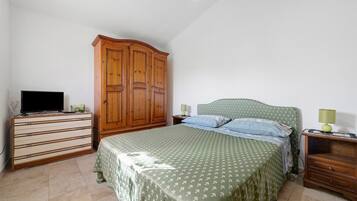 Een slaapkamer met een bed, een houten garderobe, een dressoir, een televisie en een lamp.