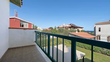 Un balcone con ringhiera verde che si affaccia su una zona residenziale con case e cielo sereno.