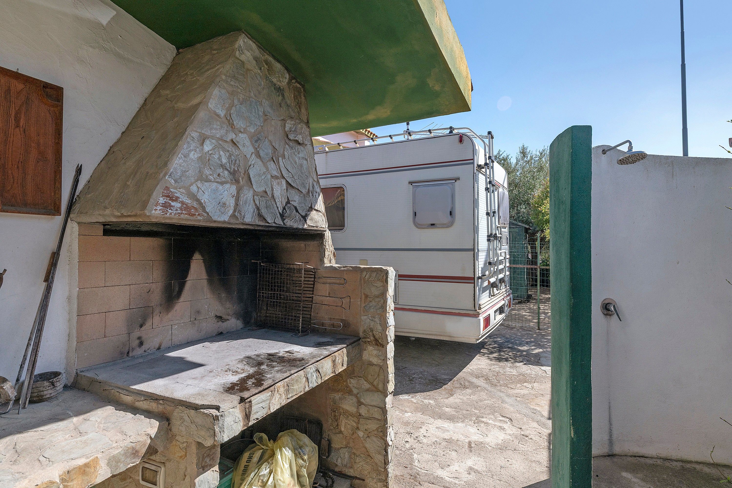 Een buitenkeuken van natuursteen met een barbecue, een tafeltje en een groen zonnescherm.